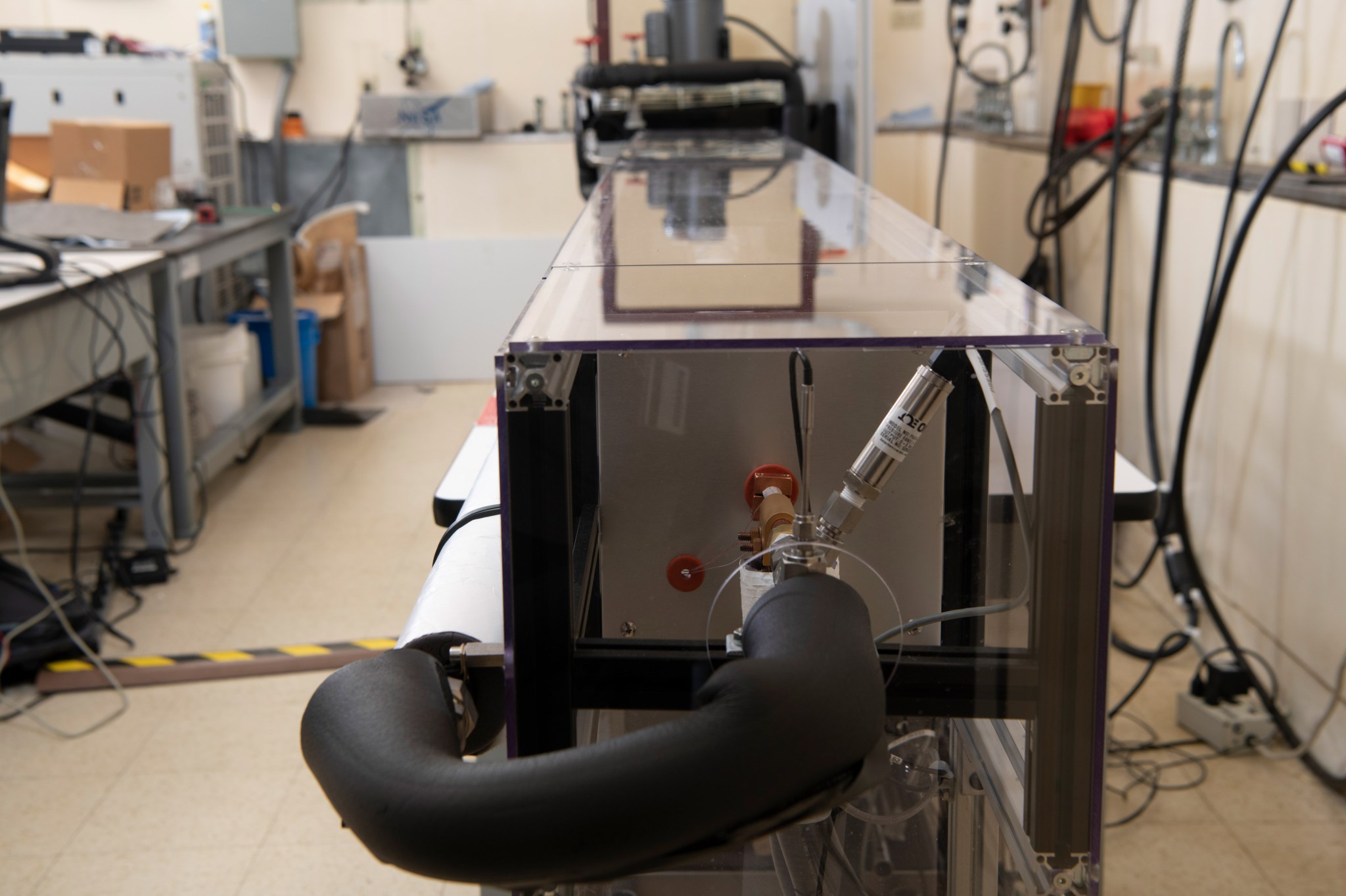 A close-up view of hardware inside a rectangular rig designed for testing wires and cables in electrified aircraft propulsion systems. The rig is surrounded by various testing machinery and equipment along the walls of the room.