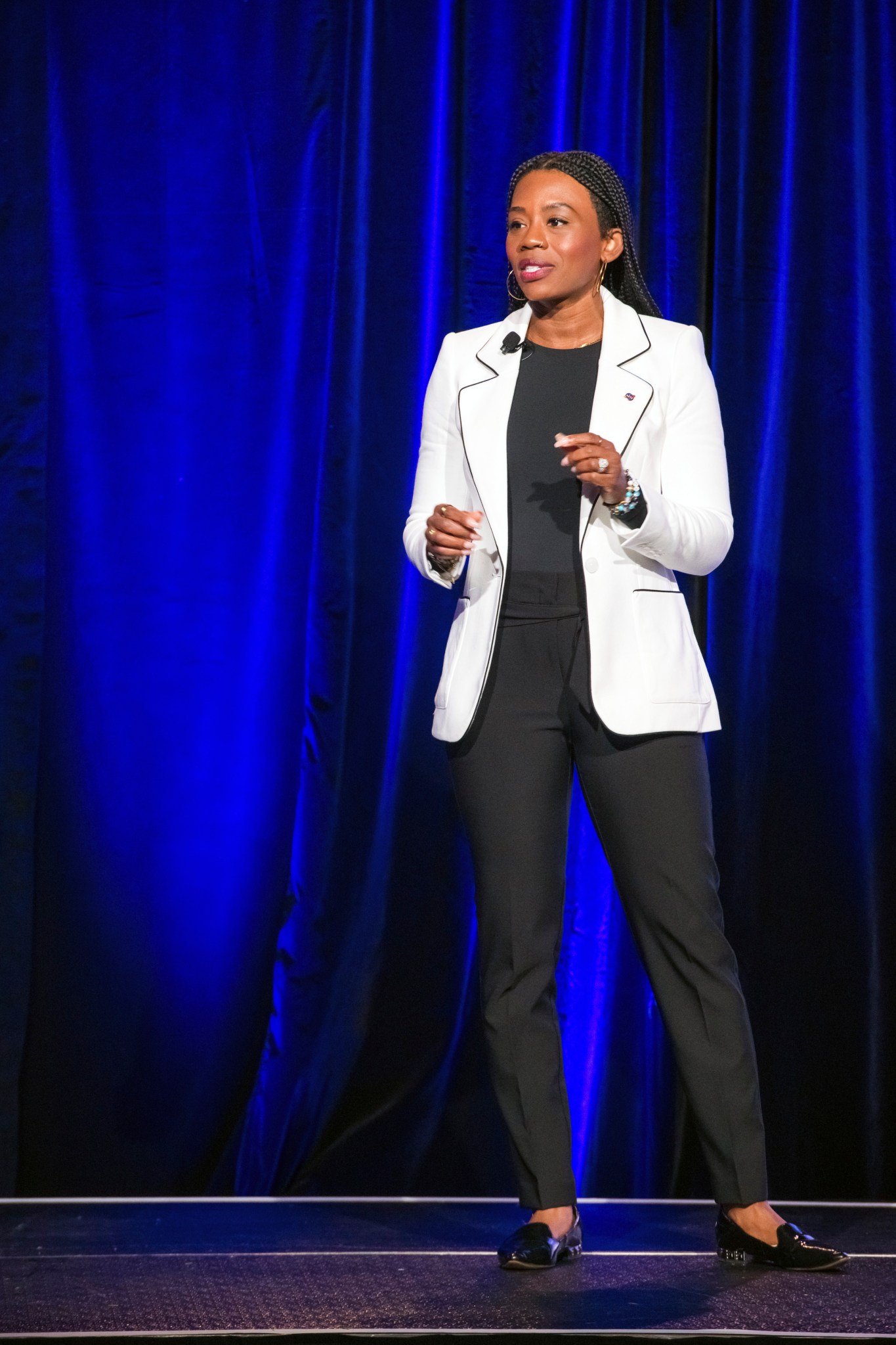 Presenter stands in front of a blue curtain and addresses audience.