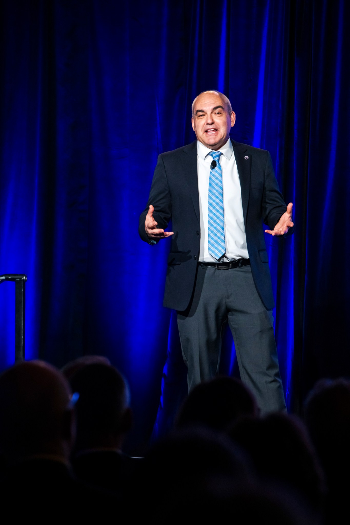Presenter stands in front of a blue curtain and addresses audience.