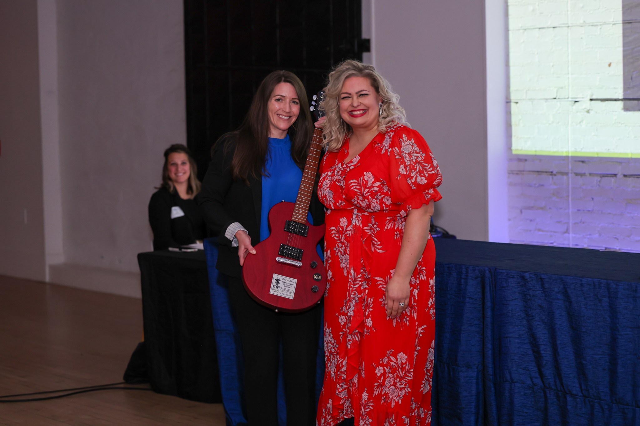 NASA Glenn Research Center’s Office of Communications director receives a red guitar from Public Relations Society of America’s Cleveland Rocks chair. One person seated in the background looks on.