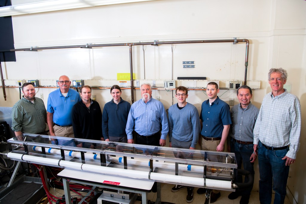 A team of nine people pose in front of a rectangular rig.