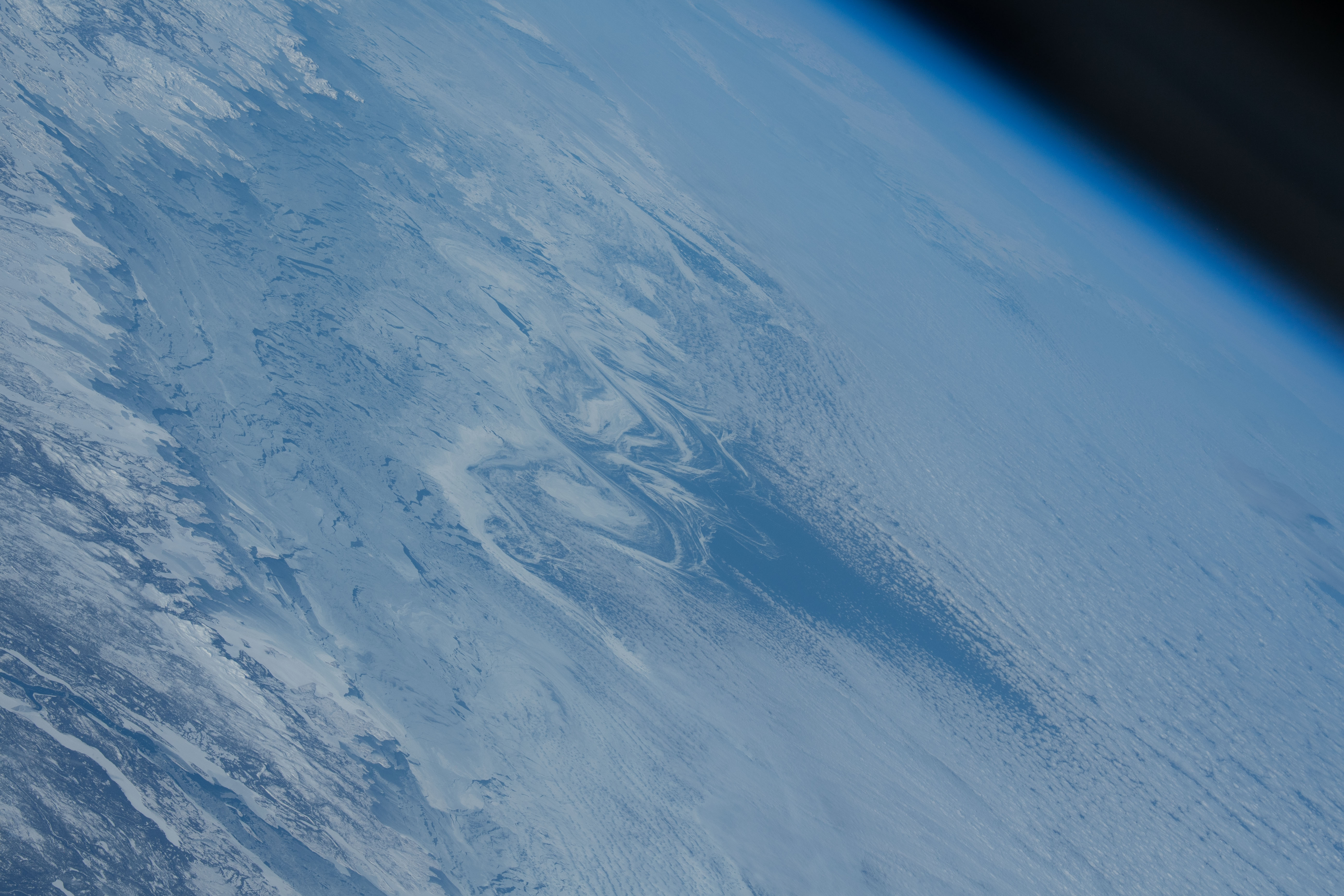 This side view of the Earth shows the ice swirls on the Atlantic Ocean in the center, and part of the planet’s atmosphere (blue) in the upper-right corner. To the bottom-left is Canada, appearing gray and snow-covered white.