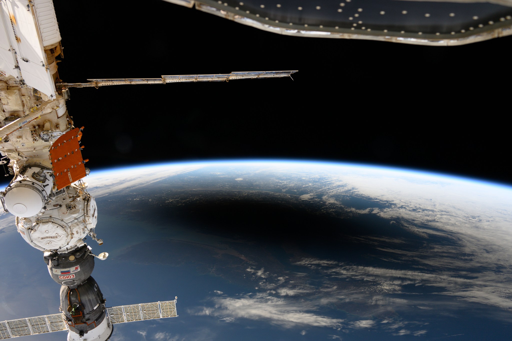 La imagen de arriba, tomada mientras la estación espacial orbitaba a más de 400 kilómetros (250 millas) por encima del Atlántico Norte, muestra la sombra oscura de la Luna creada por el eclipse sobre la superficie de la Tierra, rodeada de nubes blancas. A lo largo del borde superior del planeta, el brillante horizonte de la Tierra brilla en el límite entre la atmósfera y el espacio.