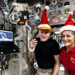 a man and a woman in Santa hats pose for a picture on the International Space Station while holding a HAM radio
