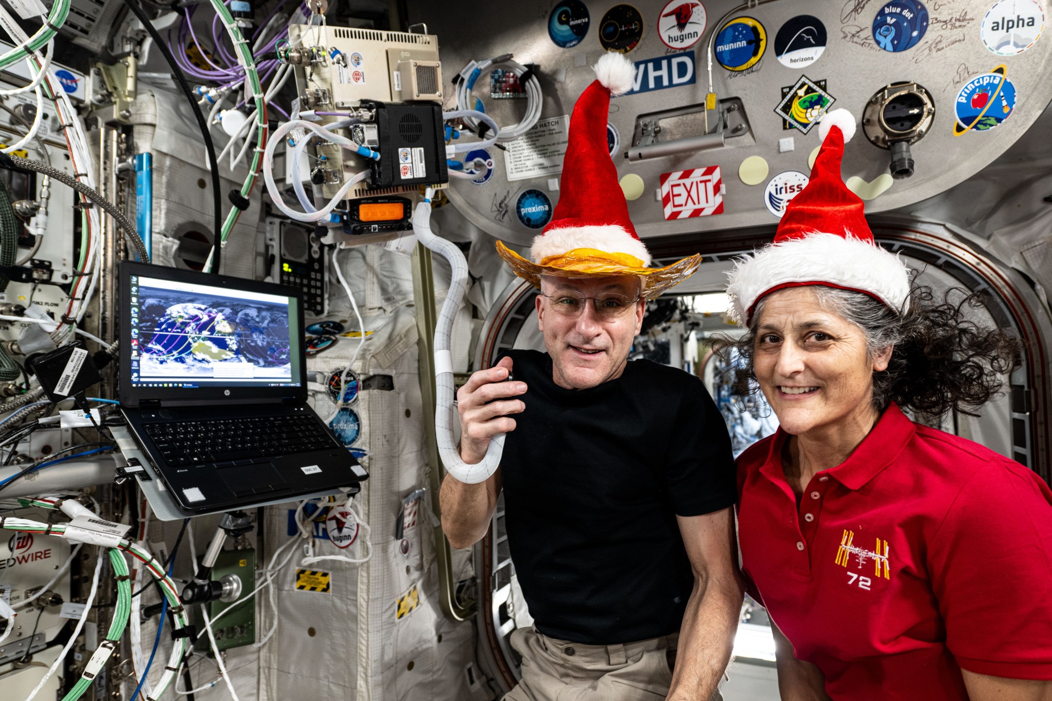 a man and a woman in Santa hats pose for a picture on the International Space Station while holding a HAM radio