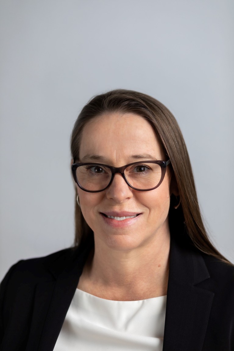 A professional portrait of a Caucasian woman with straight brown hair, brown eyes, and brown rimmed glasses.