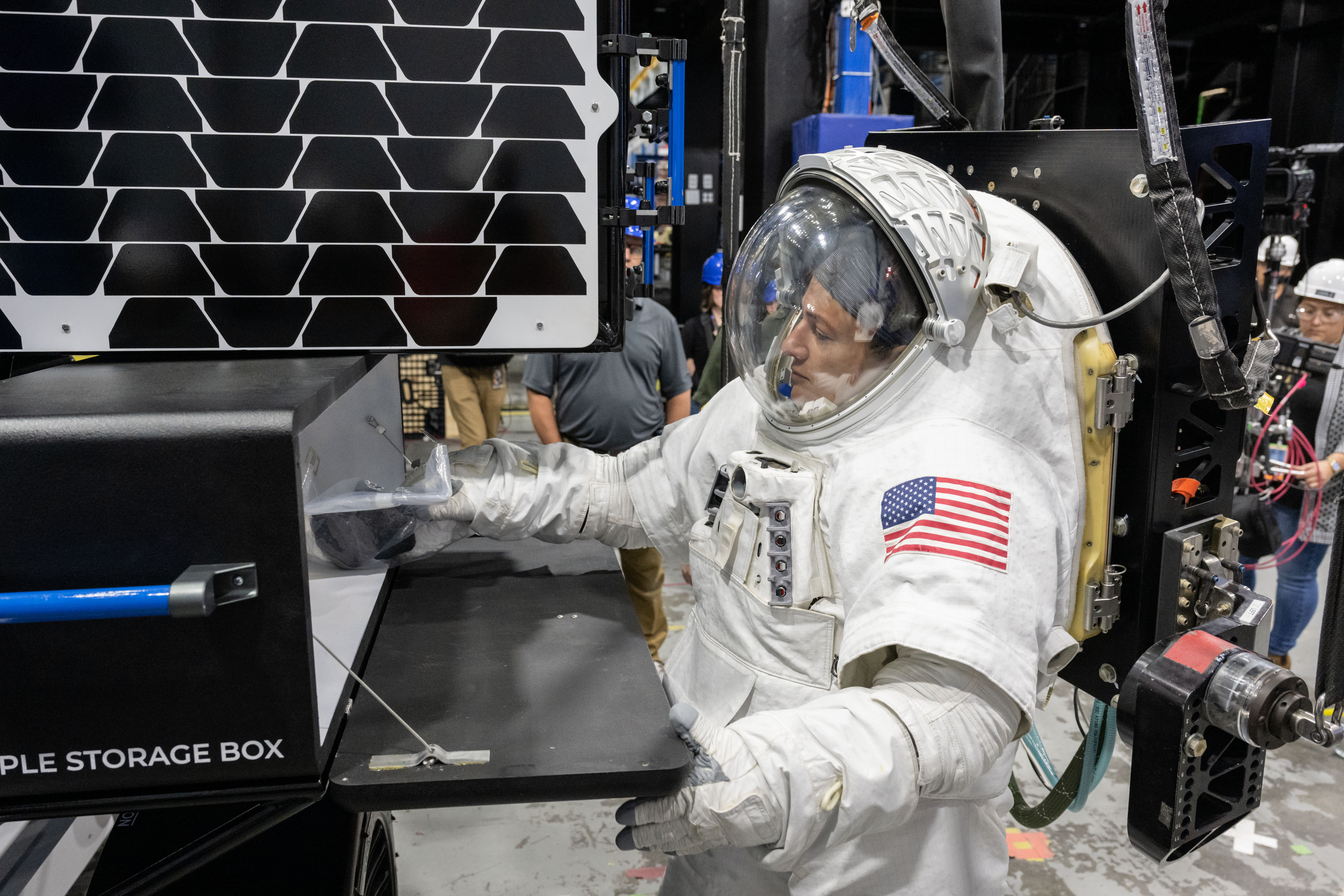 NASA astronaut Jessica Meir wearing a white spacesuit with the American flag on her left shoulder places a science sample bag inside of a black sto...