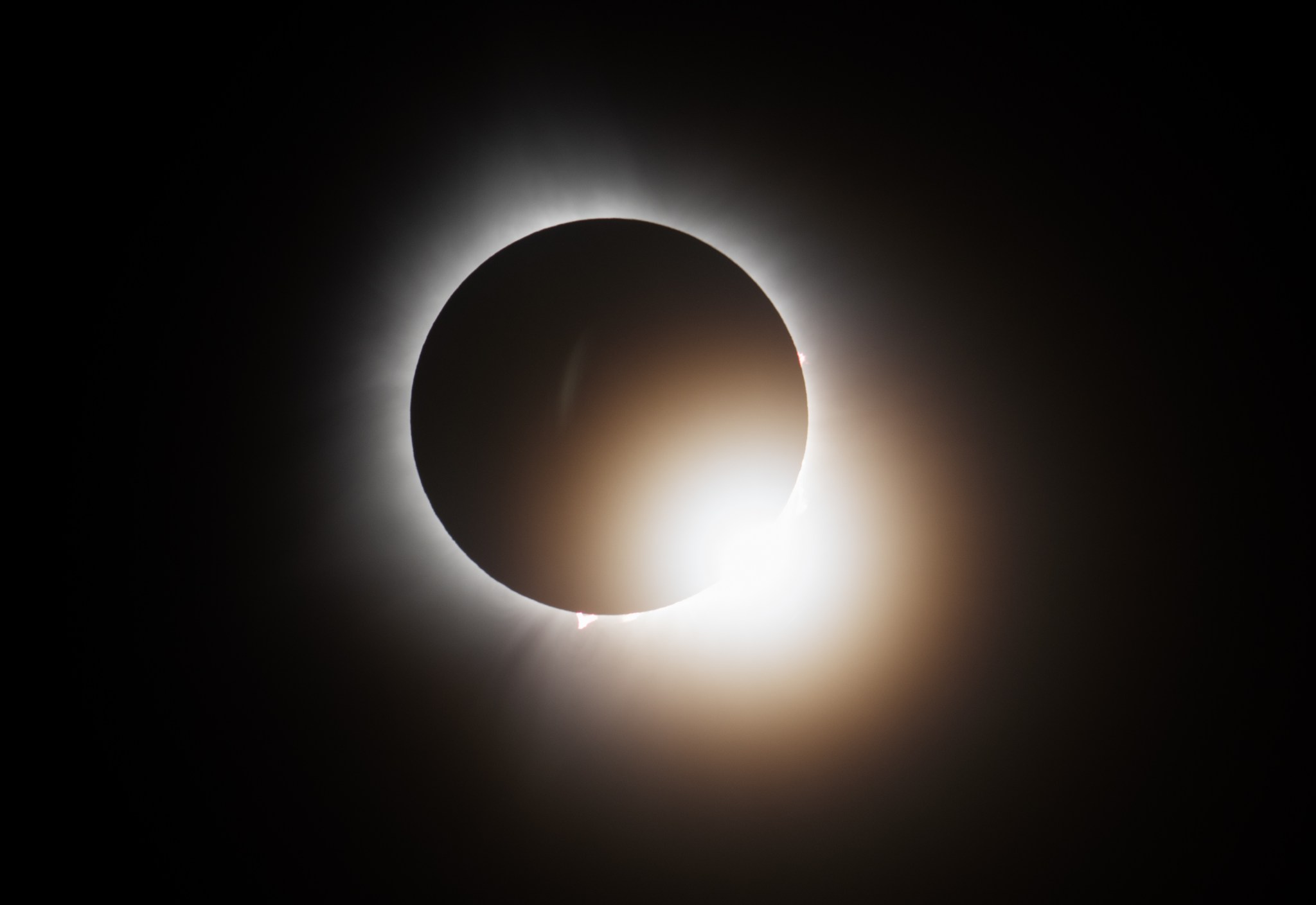 The Moon covers the Sun completely, with one last bit of brightness showing. The sky is dark all around.