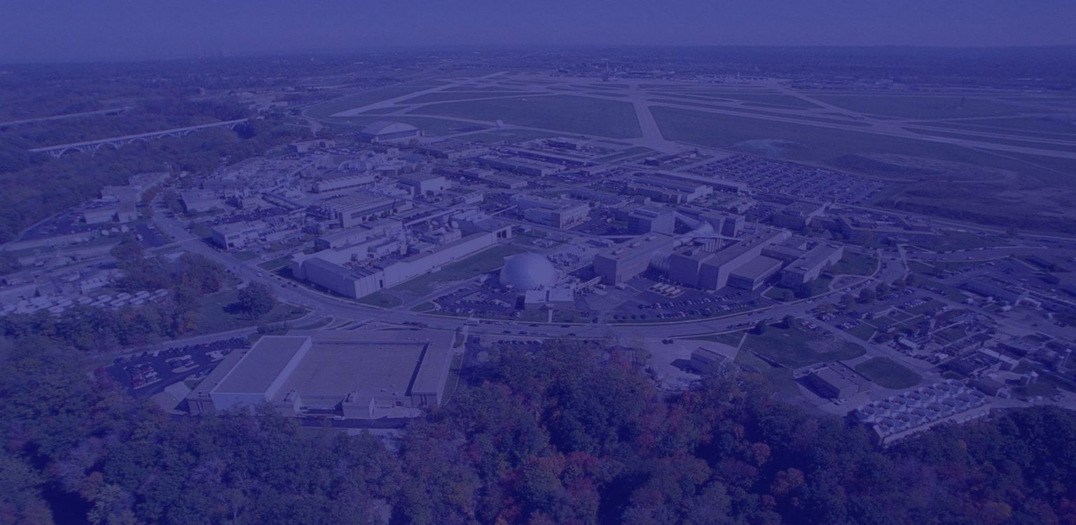 Aerial view of NASA's Glenn Research Center, showing multiple buildings, surrounding roads, parking lots, and green spaces; an airport runway is visible in the background.