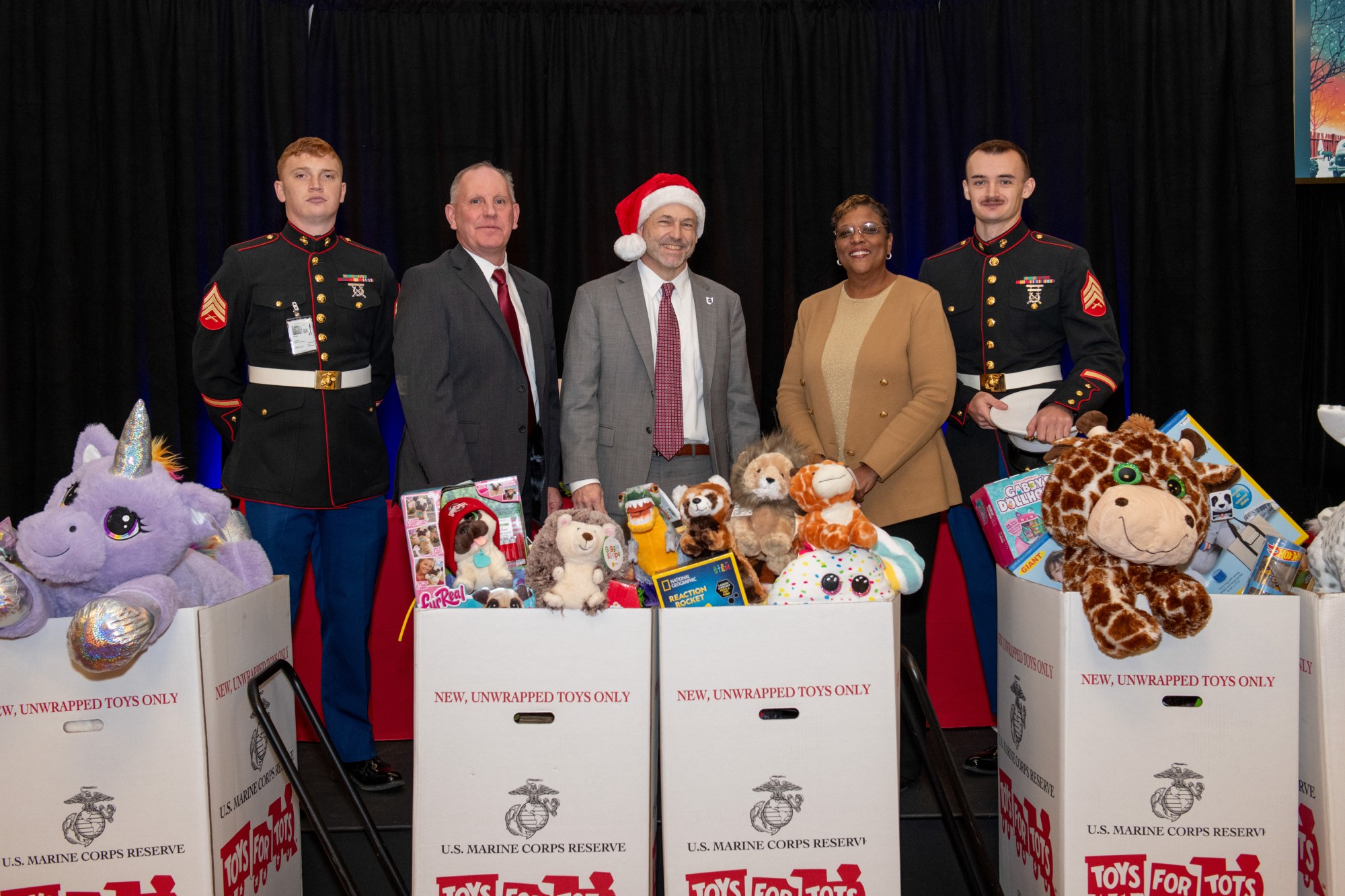 Marine Corps Reserve representatives and Glenn leadership stand in front of several large boxes filled with toys and stuffed animals.