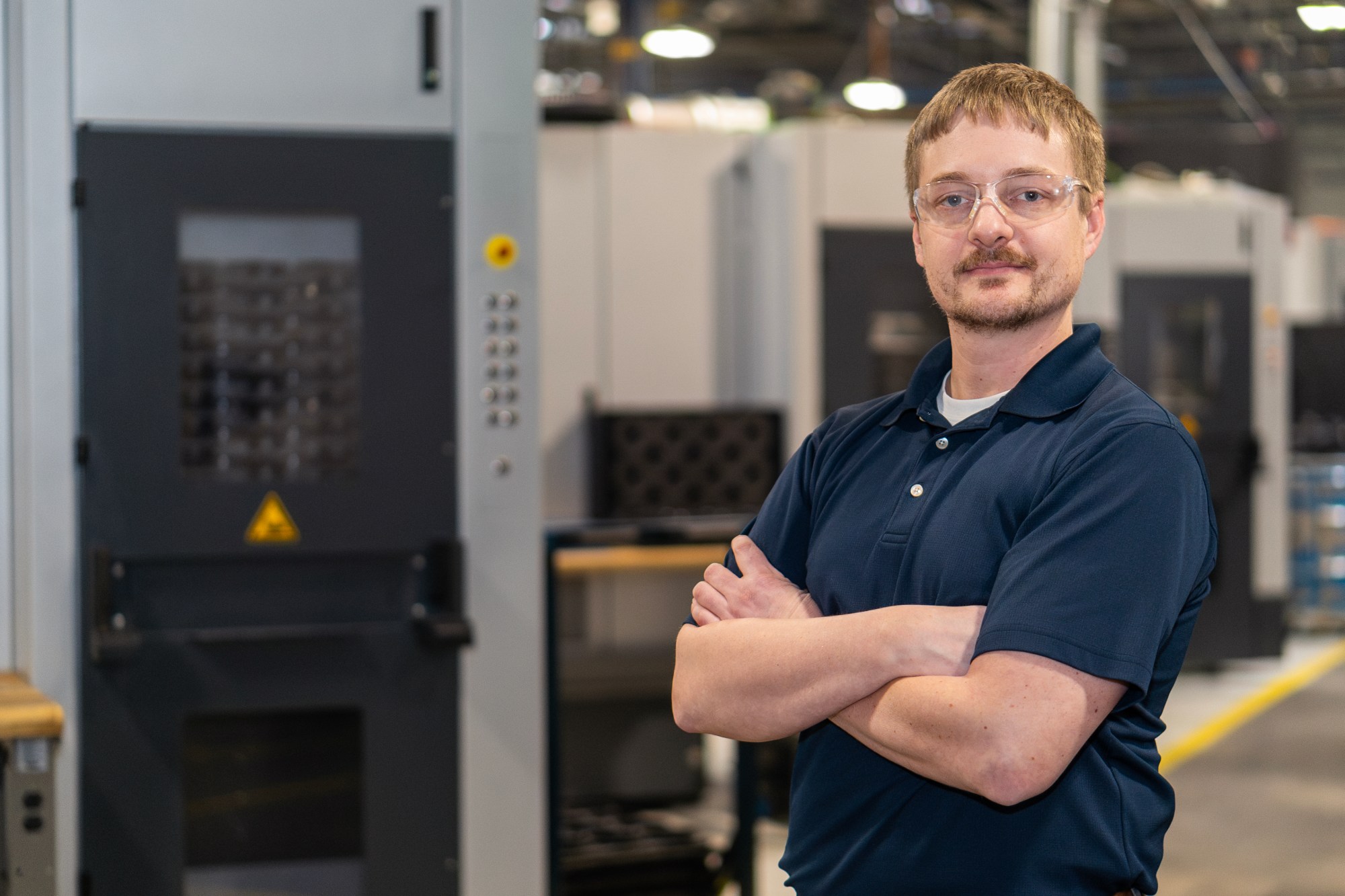 A young white man with red hair and glasses stands with his arms crossed.