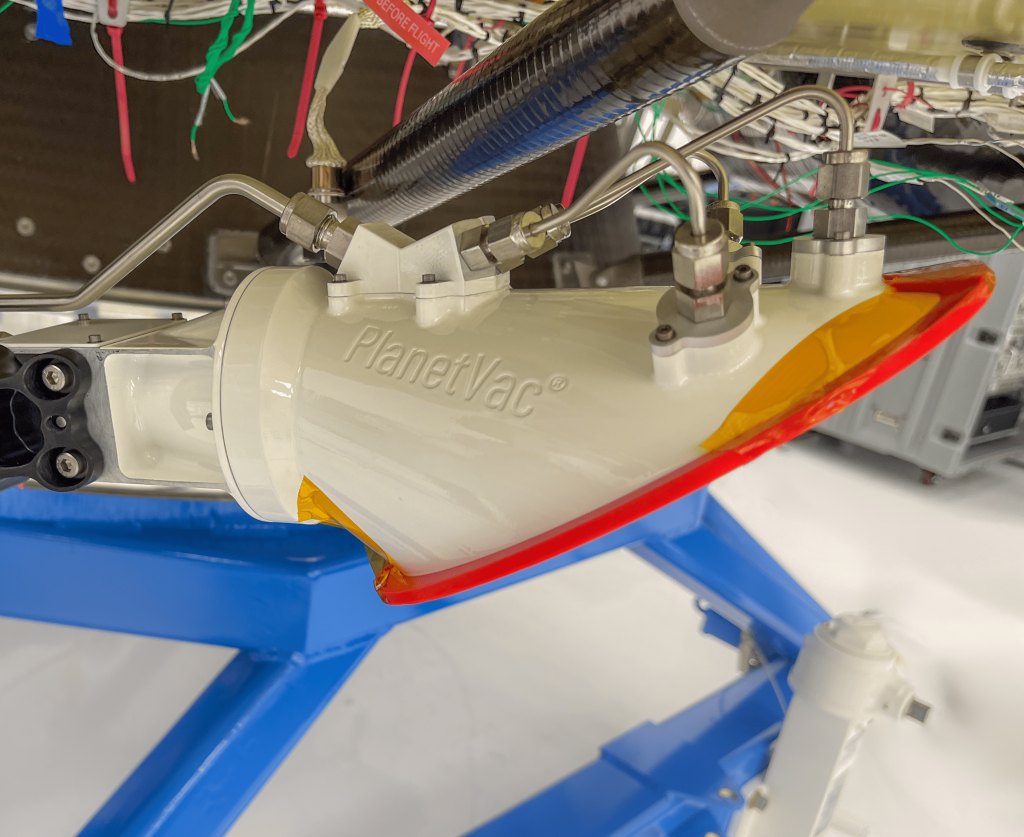 A sizable cone-shaped device with the label PlanetVac on its side is positioned on a blue area of a lander.