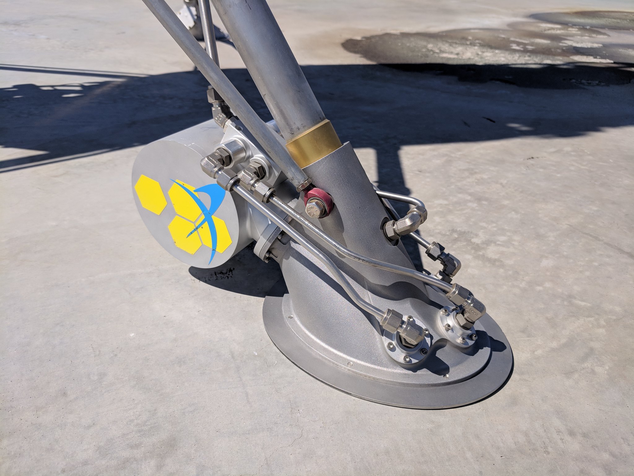 A metal pole with an oval "foot" rests on a concrete surface. Tubes run from the foot to a box on the back of the leg.