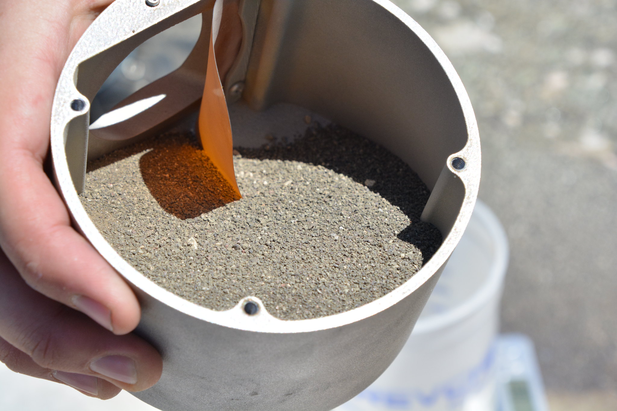 A hand is holding a cylindrical container filled with a sandy material.