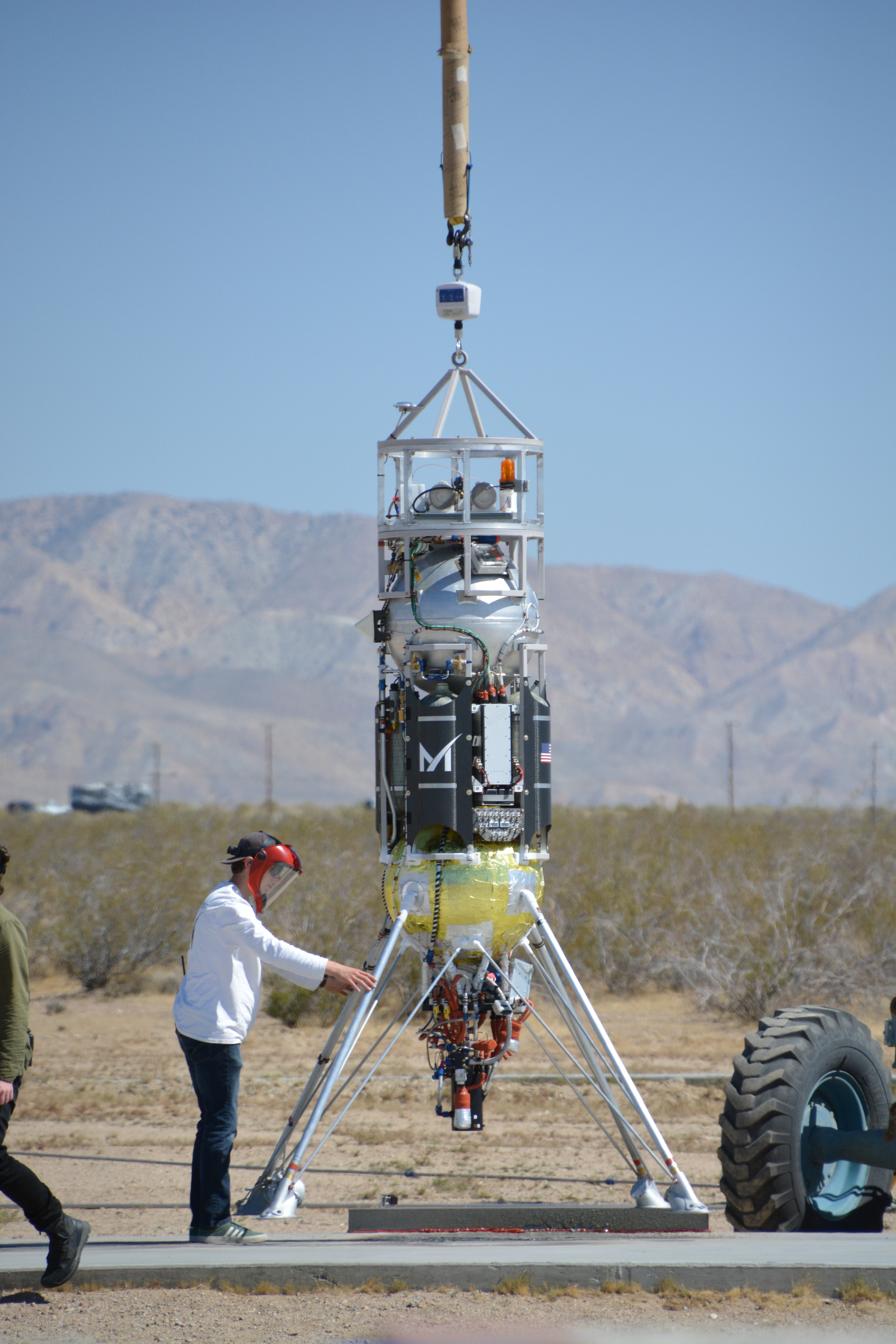 A person stands next to a vertical takeoff vertical landing craft with mountains in the background.