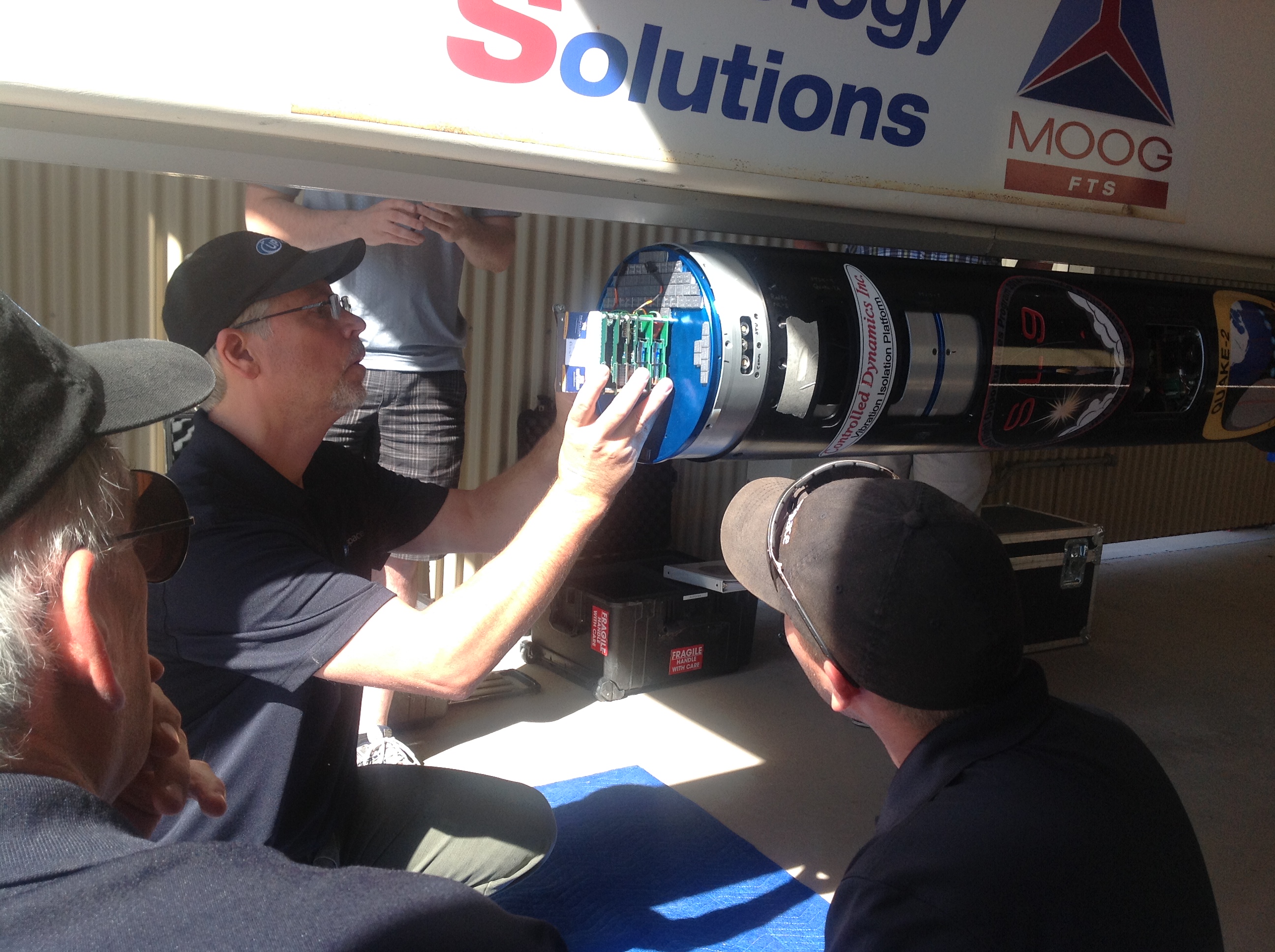 A person attaches a stack of circuit boards to the end of a tube while two other people look on.