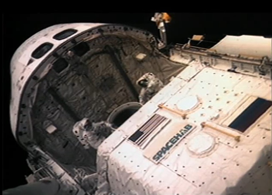 Image shows two astronauts in spacesuits in the payload bay of the space shuttle during a spacewalk.