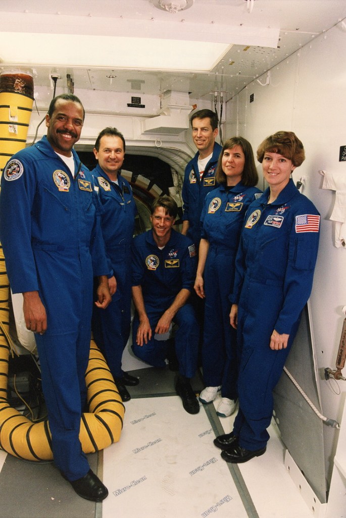 Group photo of six astronauts wearing blue flight suits.