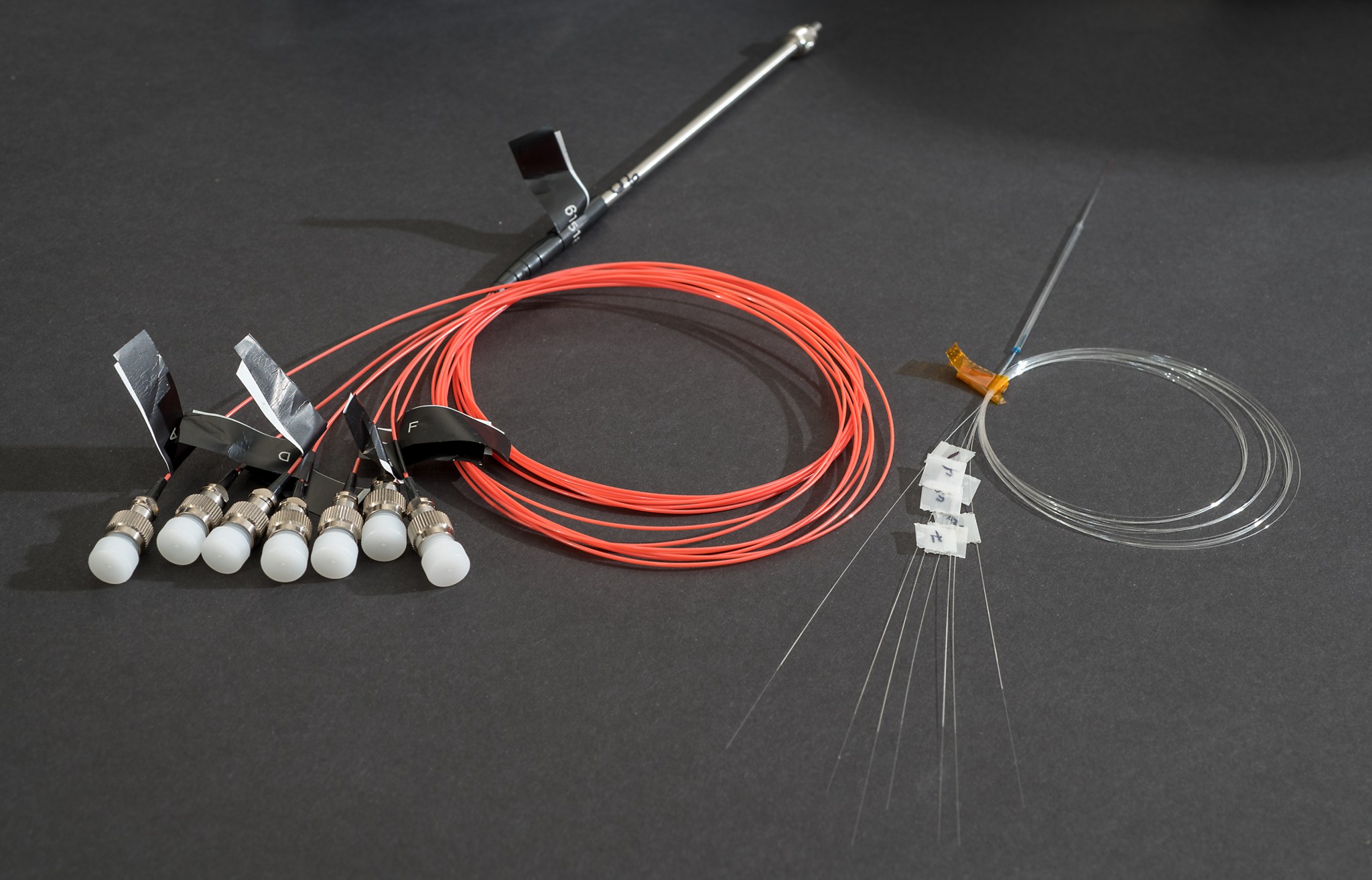 Two photonic lanterns made from optical fiber. On the left, the lantern is packaged in metal tubes and plastic; on the right the unpackaged glass lantern is shown. Both lanterns have a single input that transitions to seven outputs. 