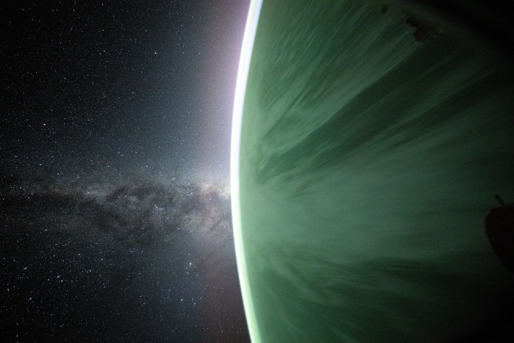 The Milky Way galaxy, filled with stars, is on the left side of the image. On the right side, Earth looks like a giant green marble with a bright curved outline (Earth's atmosphere).