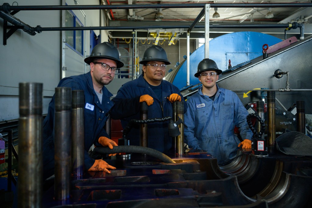 Shane Calamia, left, Mike Bungubung, center, and Nick Delurio, right, clean the oil residue from the low-end pressure air compressors that are part of the Unitary Plan Wind Tunnel (UPWT), during a tear down for maintenance in building N268.