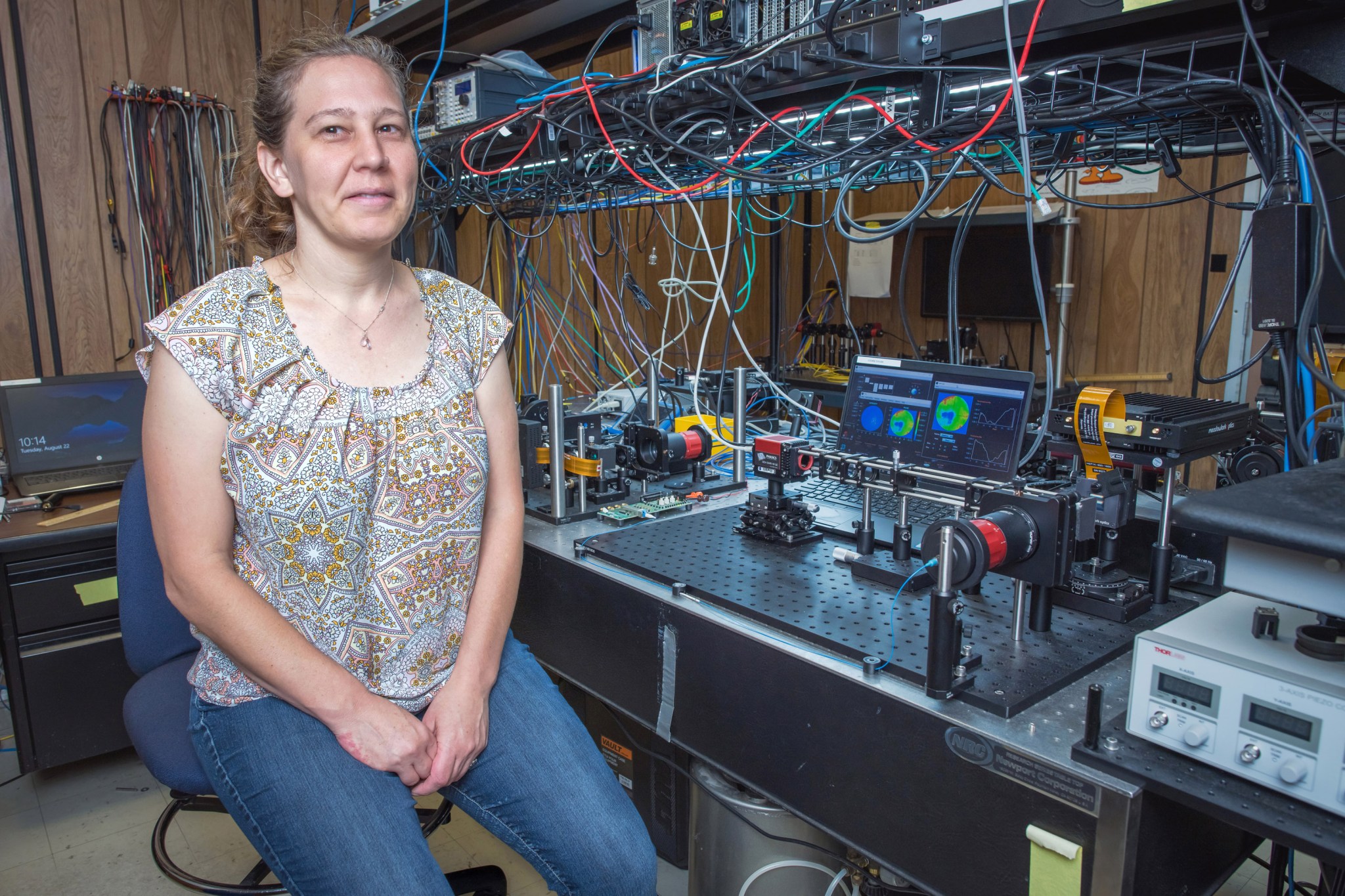 Sarah Tedder sits next to an optical table with an optical setup of optical components on a bread board.  