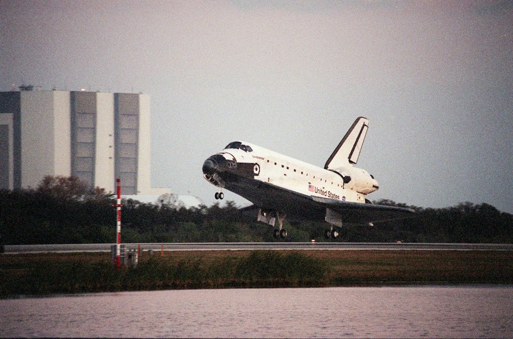 Image of a space shuttle landing in Florida, with a large building in the background.
