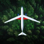 A top view of a truss-braced wing commercial aircraft flying over a forest of green trees.
