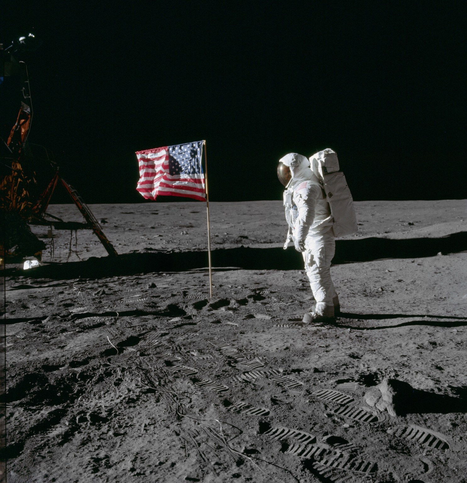 Astronaut Edwin E. Aldrin Jr., lunar module pilot of the first lunar landing mission, poses for a photograph beside the deployed United States flag during an Apollo 11 extravehicular activity (EVA) on the lunar surface. The Lunar Module (LM) is on the left, and the footprints of the astronauts are clearly visible in the soil of the moon. Astronaut Neil A. Armstrong, commander, took this picture with a 70mm Hasselblad lunar surface camera. While astronauts Armstrong and Aldrin descended in the LM, the "Eagle", to explore the Sea of Tranquility region of the moon, astronaut Michael Collins, command module pilot, remained with the Command and Service Modules (CSM) "Columbia" in lunar orbit.