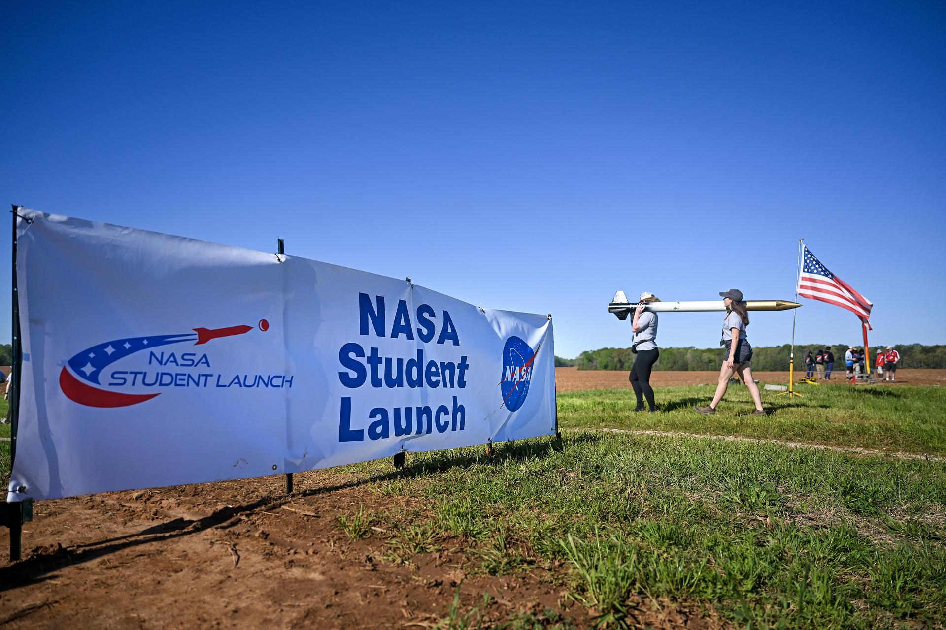 A NASA Student Launch sign with two people walking and carrying a rocket on their shoulders