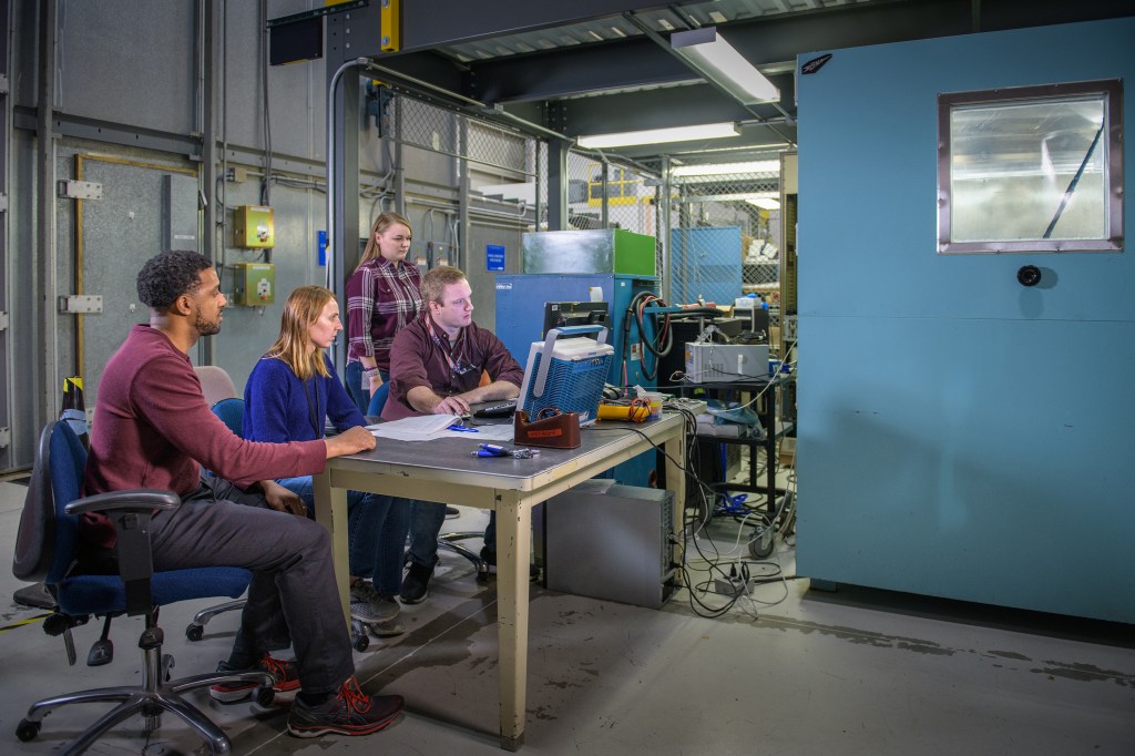 Four researchers gather around a table as they collect data during thermal tests of a cruise motor controller designed for future electrified aircraft propulsion.