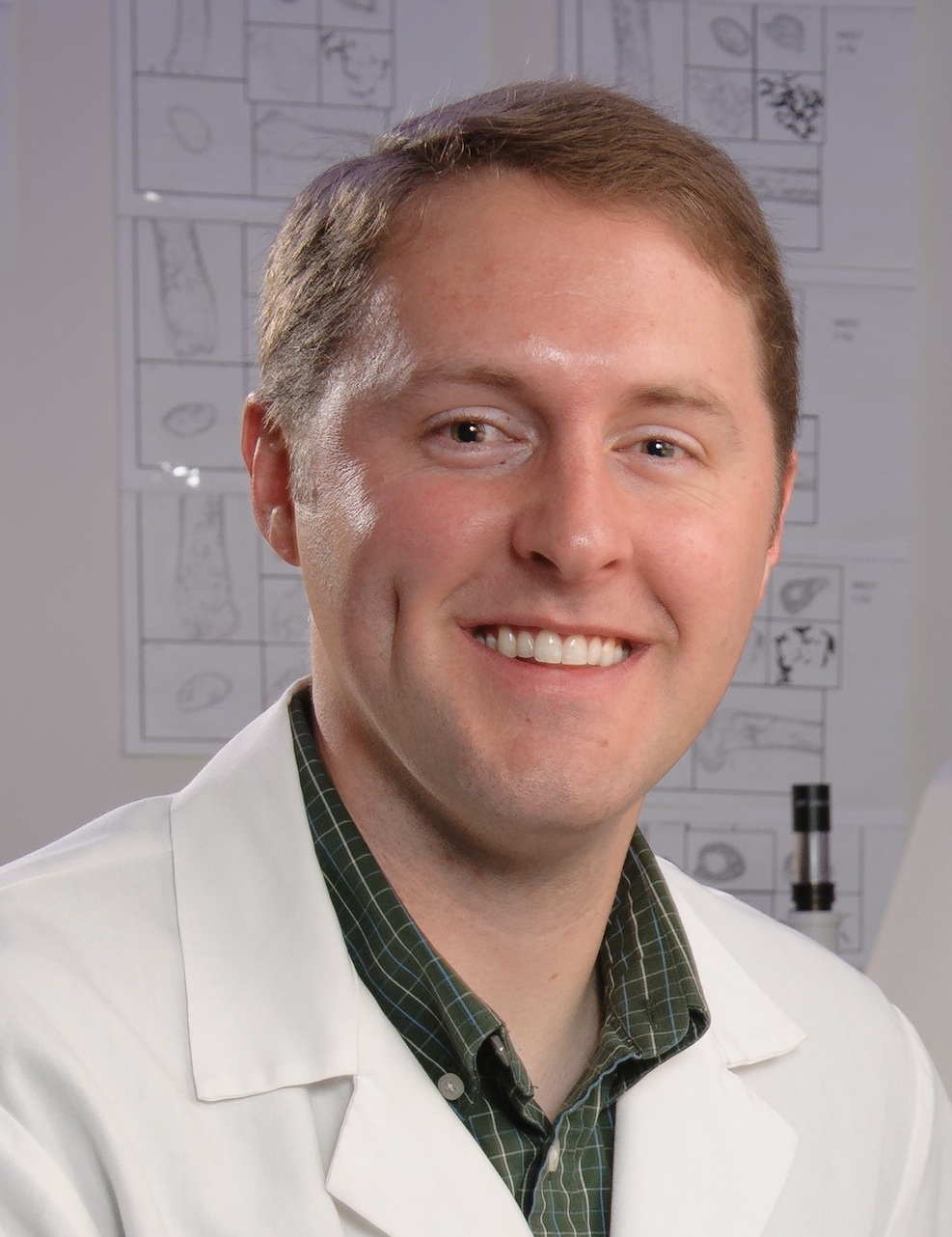 Portrait photo of space bioscientist Josh Alwood of NASA Ames Research Center. He is sitting in a laboratory wearing a white lab coat.