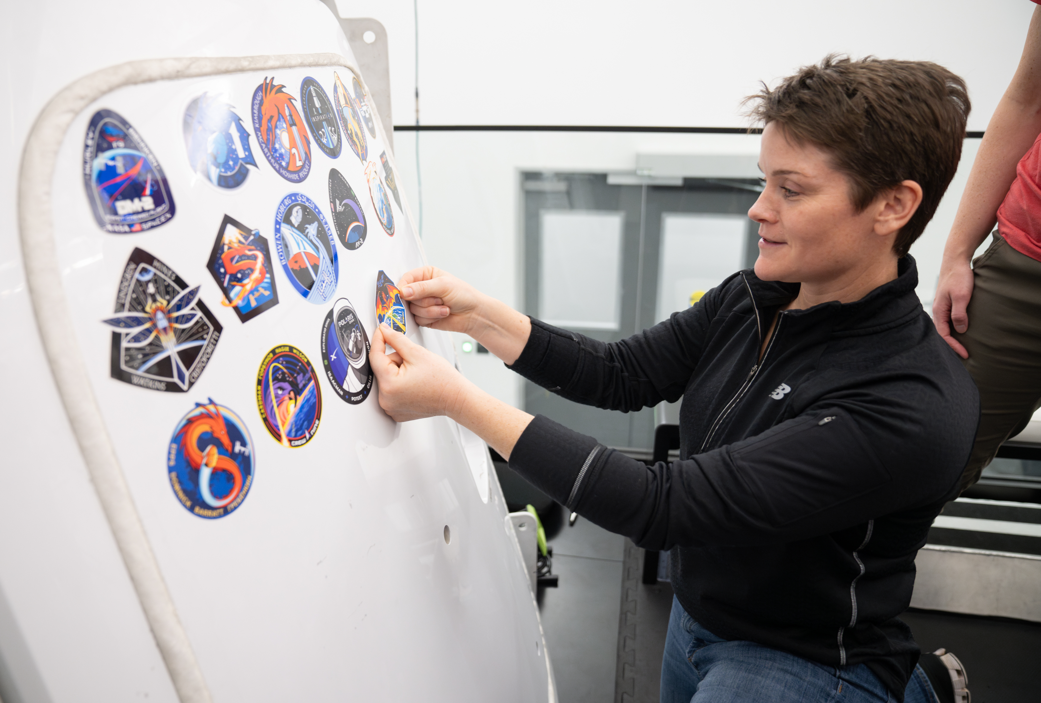 NASA astronaut and commander of NASA's SpaceX Crew-10 mission Anne McClain places the Crew-10 mission patch on the Dragon training spacecraft at the company’s facility in Hawthorne, California.