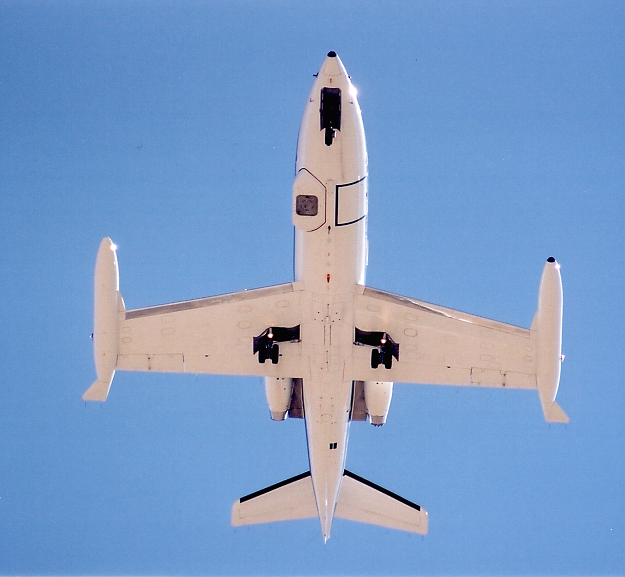 A view of the underside of a flying white aircraft set against a clear blue sky.