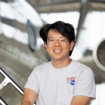 Portrait photo of scientists Sam Kim of NASA Ames Research Center, sitting in front of an aircraft inside a hanger.