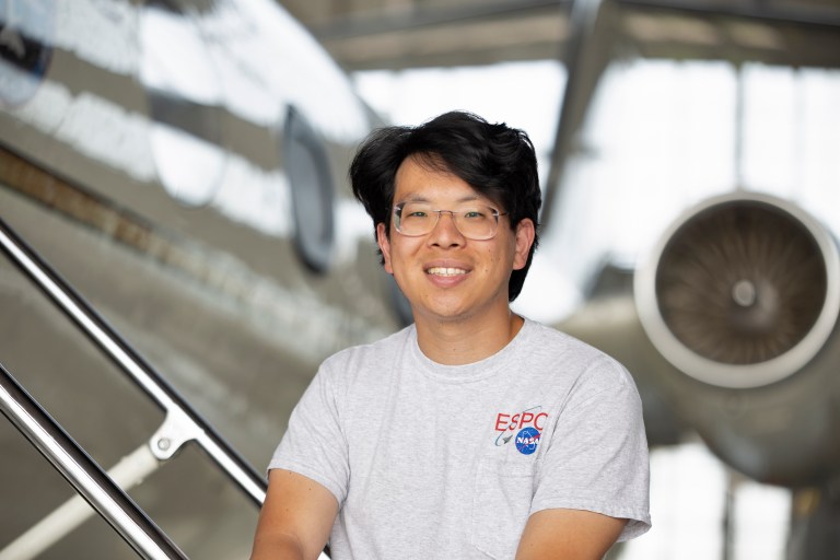 Portrait photo of scientists Sam Kim of NASA Ames Research Center, sitting in front of an aircraft inside a hanger.