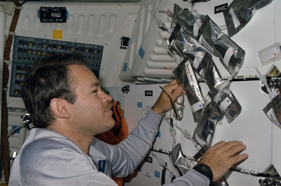 View of an astronaut aboard a space shuttle arranging silver colored drink bags.