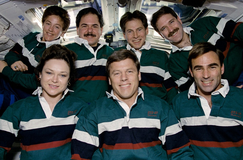 Group photo of seven astronauts, three in front and four in back, on the shuttle's flight deck.