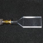 Photograph of a plastic scintillator block attached to a small detector set against a black background.