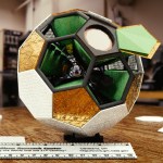 Computer-generated image of a detectors arranged in a ball set on wood bench top in a laboratory with covers and a ruler for scale.
