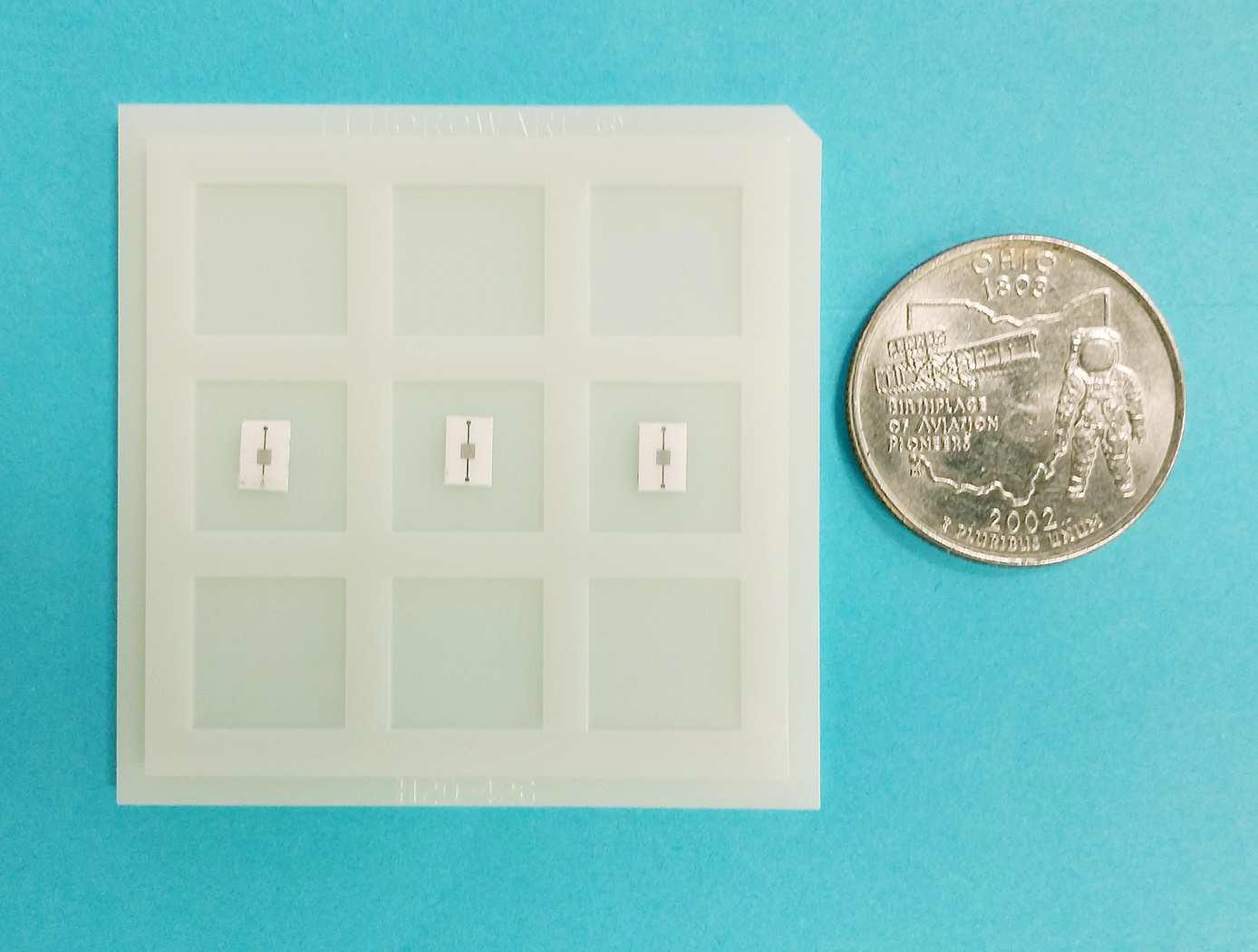 A grid with three small electronic components is displayed next to an Ohio state quarter for scale, all on a blue background.