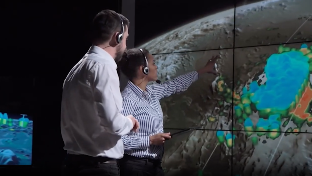 Digital Future video screen shot of a man and a woman looking at a large screen showing earth's terrain.