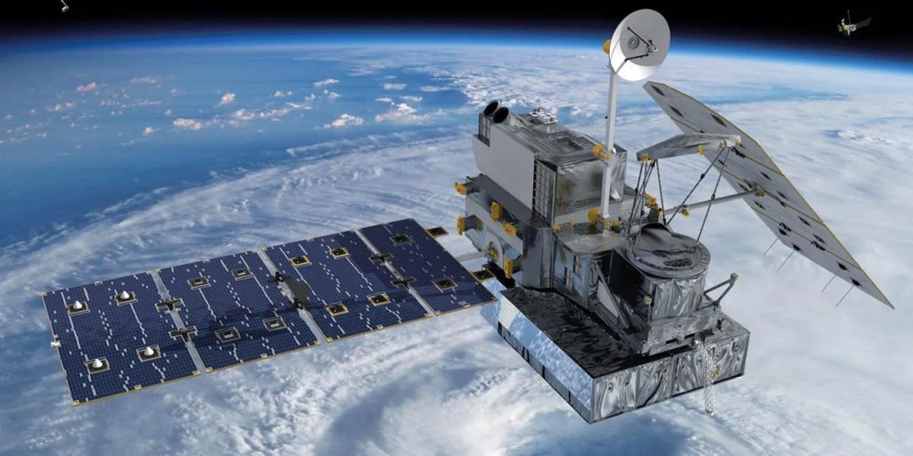 An artist’s concept of an observational satellite. Its rectangular body is made up of white, gray, and yellow instruments, and some parts are covered in shiny silver foil. A white satellite dish is propped up on a pole in the spacecraft’s center. Two solar panels are attached to the satellite’s body: a straight blue solar panel on its left, and a diagonally tilted solar panel on its right with only its white underside visible. The spacecraft is positioned over a blue planet with white clouds, though a dark, expansive space can still be seen near the image’s top edge.