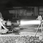 Kneeling photographer films ramjet engine firing at night.