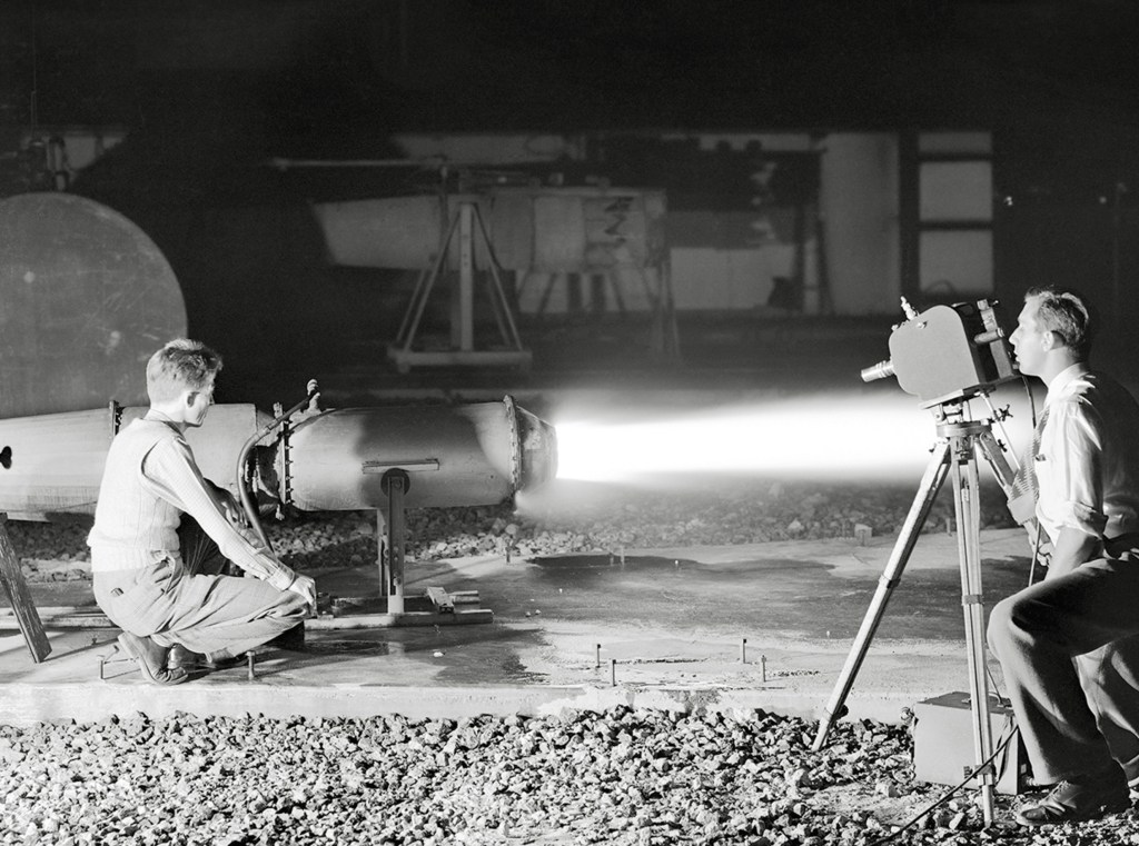 Kneeling photographer films ramjet engine firing at night.