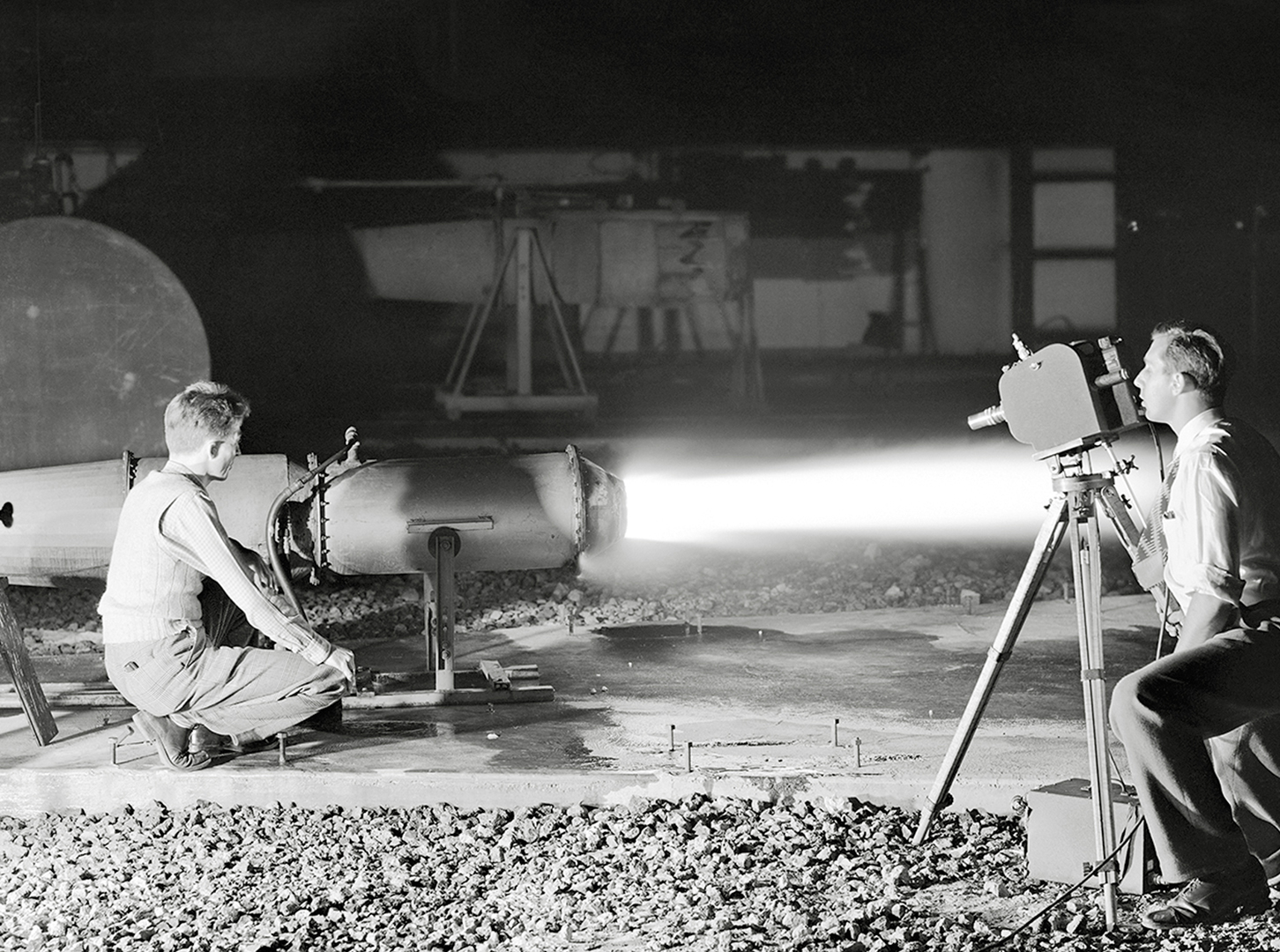 Kneeling photographer films ramjet engine firing at night.