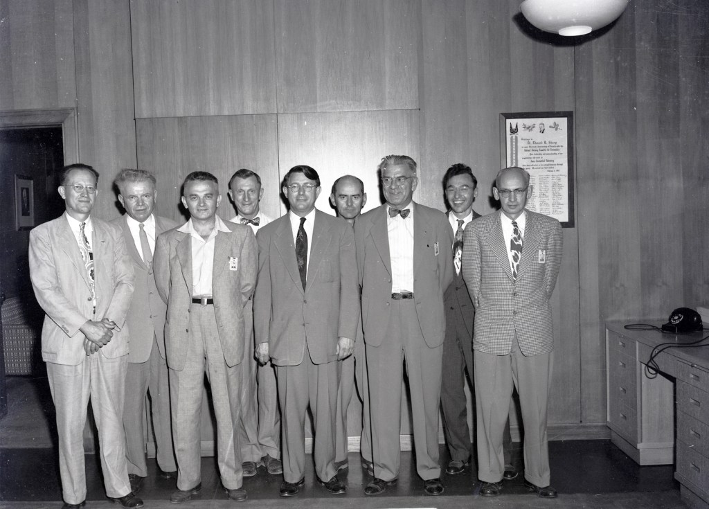 Group of men standing against office wall.