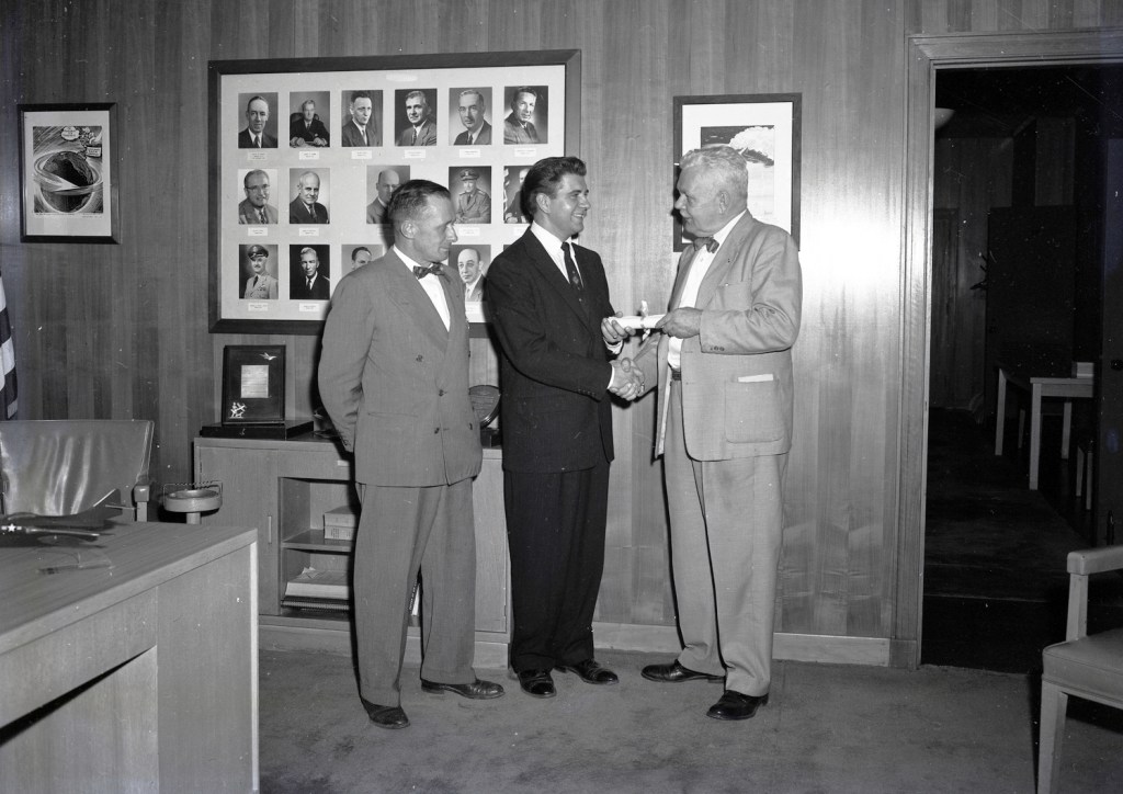 Three men standing in office.