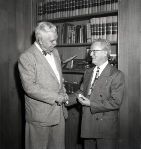 Two men shaking hands in front of bookcase.