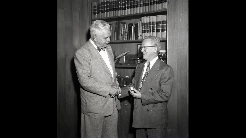 Two men shaking hands in front of bookcase.